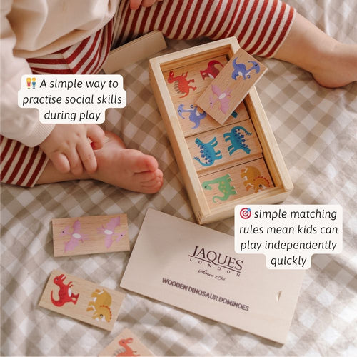 Children playing with wooden dinosaur dominoes set on a checkered blanket, with Jaques of London branding. 