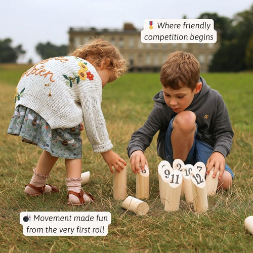 Two children playing with numbered wooden stakes in a grassy field. 