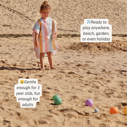 A child plays in a sandy area, appearing to toss or roll a ball. 