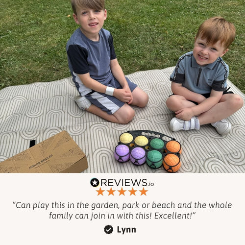 A young boy sits outdoors with a set of colorful boules/pétanque balls spread around him. 