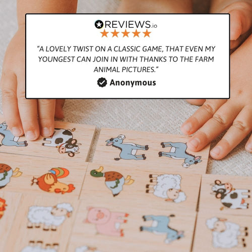 A close-up of a child's hands arranging wooden animal puzzle tiles on a light fabric surface. A large white review card overlay at the top reads a positive anonymous review with stars and text, and the product pieces show cartoon animals such as a cow, goat, sheep, pig, chicken, and donkey. 