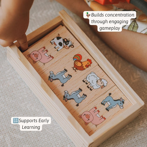 A wooden farm animal sorting or matching toy box shown on a textured fabric surface, with a child's hand and arms visible around it. The box contains illustrated animal pieces including a pig, cow, rooster, sheep, and donkey. 