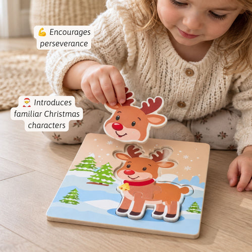 A young child in a cream knit sweater is playing with a wooden Christmas reindeer puzzle on a light wood floor. The child is placing a reindeer piece onto a winter-themed board with other pieces.
