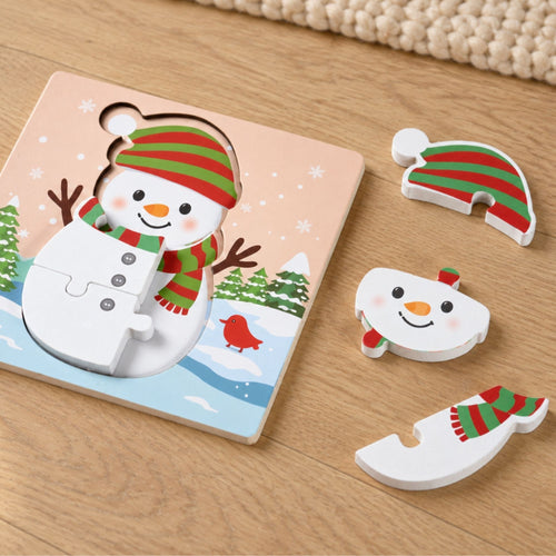 A children's wooden snowman puzzle set on a light wood tabletop. The square puzzle board shows a smiling snowman wearing a red and green striped hat and scarf with a winter landscape beneath.
