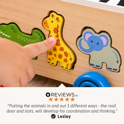 A close-up of a wooden animal puzzle box being used by a child's hand, with a yellow giraffe piece being pushed into place. Other visible pieces include a green crocodile and a blue elephant.