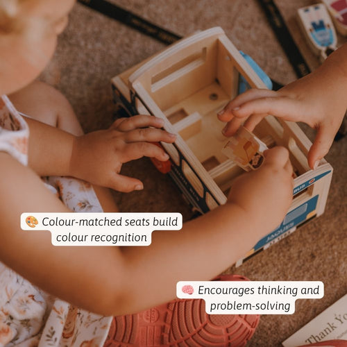 A child's hands and part of their body are shown interacting with a wooden toy bus while sitting on a carpeted floor. The toy has light natural wood seats and blue side panels, with overlaid text describing its educational benefits. 