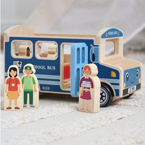 A wooden toy school bus with blue sides and natural wood body, plus small wooden character figures standing beside it on a soft white textured surface. 