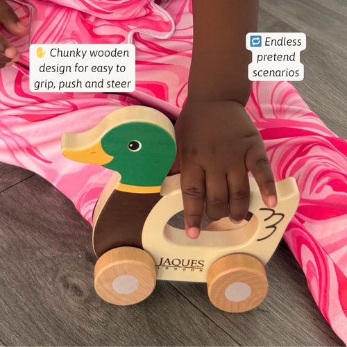 Child playing with a wooden duck toy on a pink blanket 