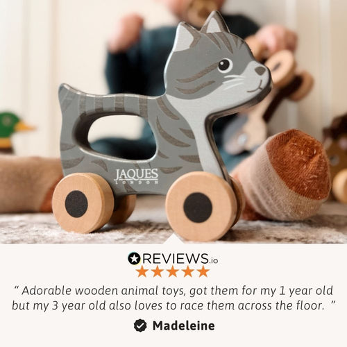 Wooden toy cat with wheels on a surface, with a blurred background of people and toys. 