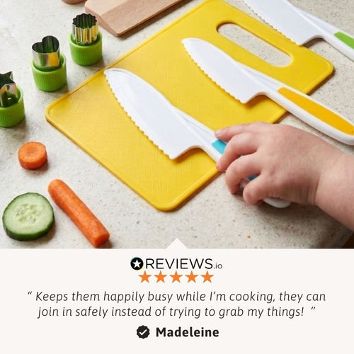 Child's hand holding a knife on a yellow cutting board with vegetables and kitchen tools. 