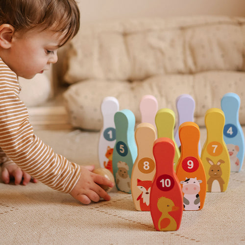 Child playing with a set of colorful wooden bowling pins with numbers and animal illustrations. 