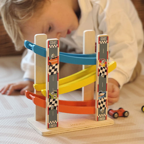 Child playing with a wooden toy race track set on a table. 