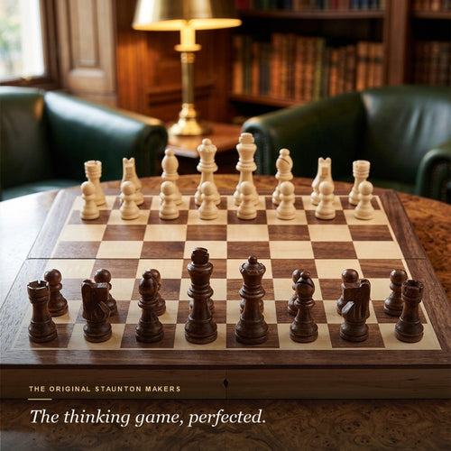Jaques folding chess set set up ready to play in a lamplit library with green leather armchairs 
