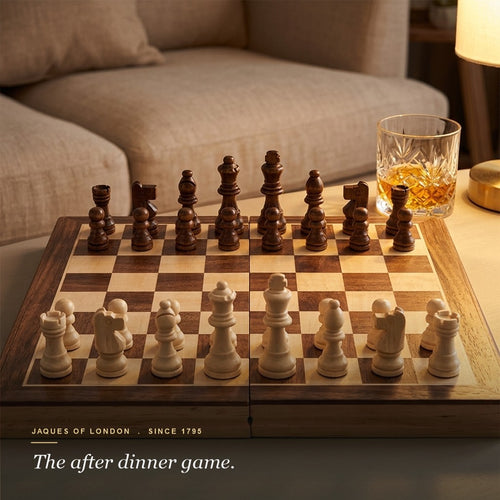 Jaques folding walnut and sycamore chess set set up on a burlwood coffee table with whisky, warm lounge behind 