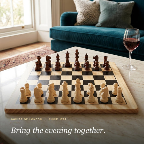 Jaques Staunton wooden chess set set up in the starting position on a marble table with red wine and a velvet sofa 