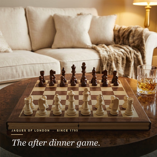Jaques folding chess set set up on a burlwood coffee table with whisky in a warm lounge 