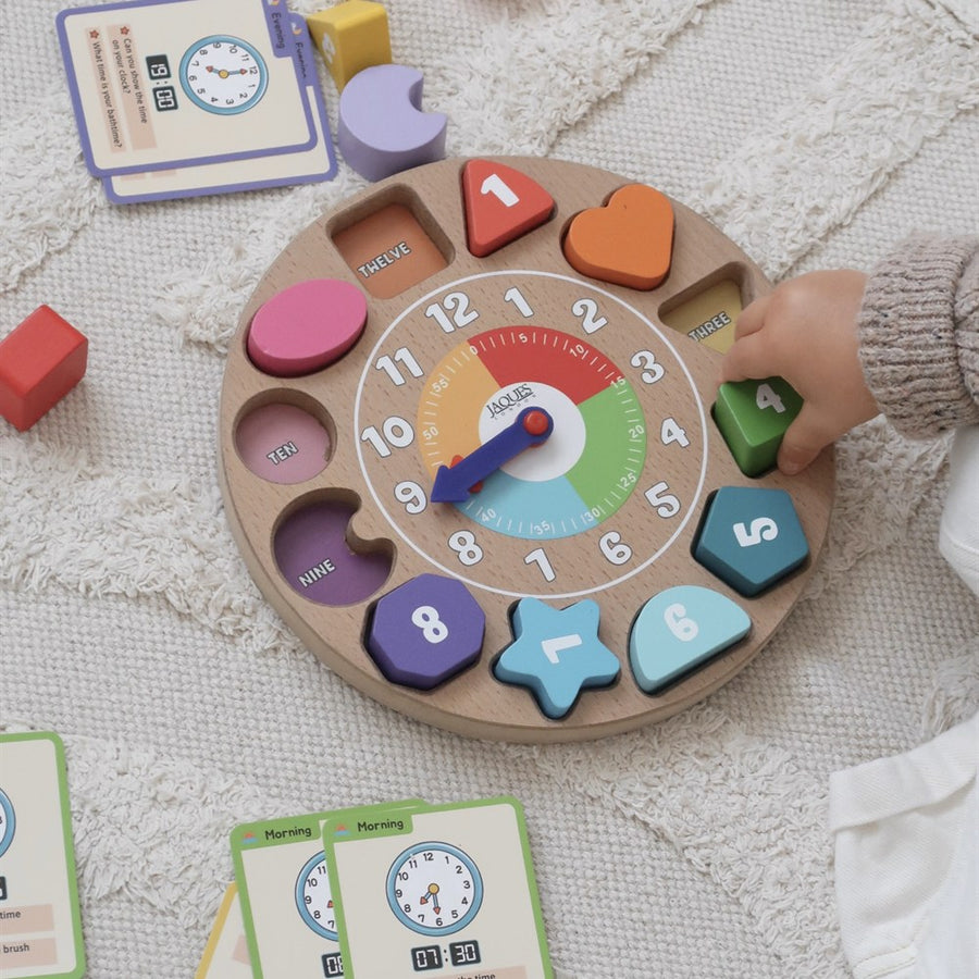 Childs hand placing the number four shape into the Jaques wooden shape sorting clock toy [fill]